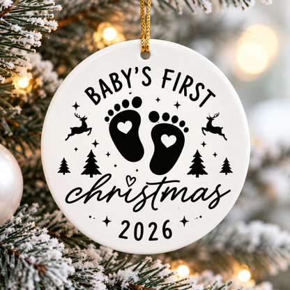 Baby's First Christmas 2026 white ceramic ornament with black baby footprints, hearts, reindeer and Christmas trees hanging on a Christmas tree