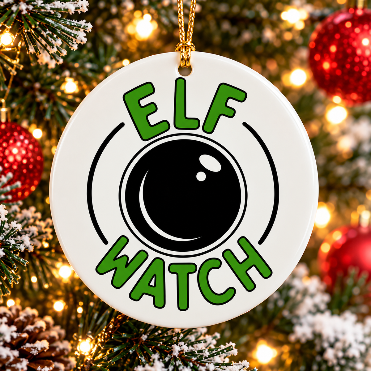White ceramic Elf Watch Christmas ornament with green lettering, black camera lens design and gold hanging cord displayed on a Christmas tree