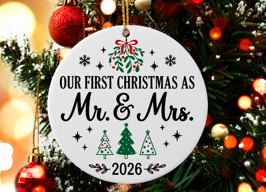 White ceramic Our First Christmas as Mr and Mrs 2026 ornament with festive Christmas trees and gold hanging cord displayed on a Christmas tree
