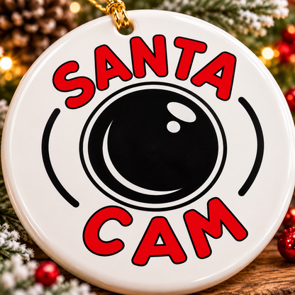 Close-up of Santa Cam white ceramic Christmas ornament featuring bold red lettering, black camera lens design and gold hanging cord