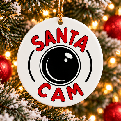 White ceramic Santa Cam Christmas ornament with red lettering, black camera lens design and gold hanging cord on a Christmas tree